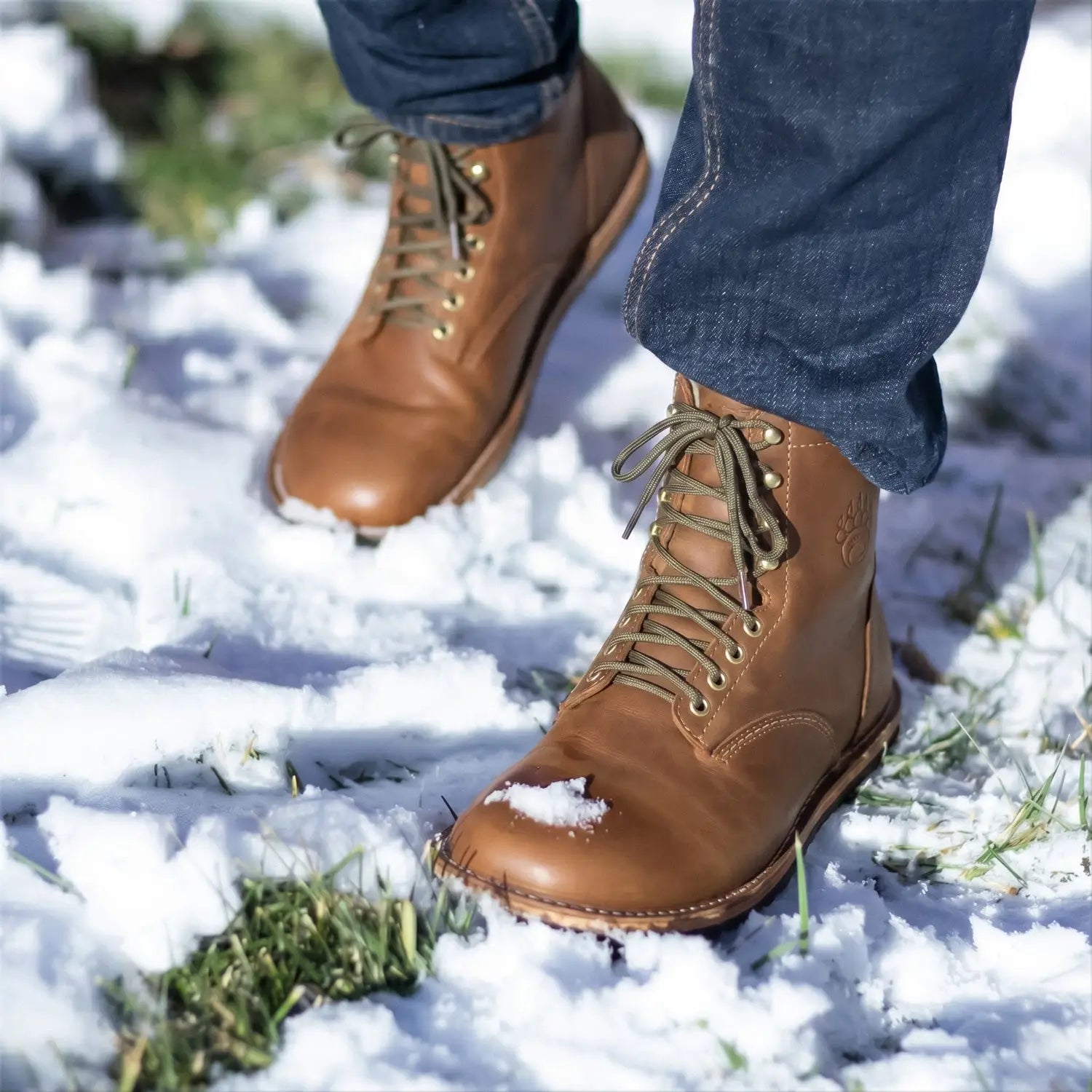 Brown leather arktos crazy horse winter-ready barefoot boot with gold eyelets and merino wool on snowy ground