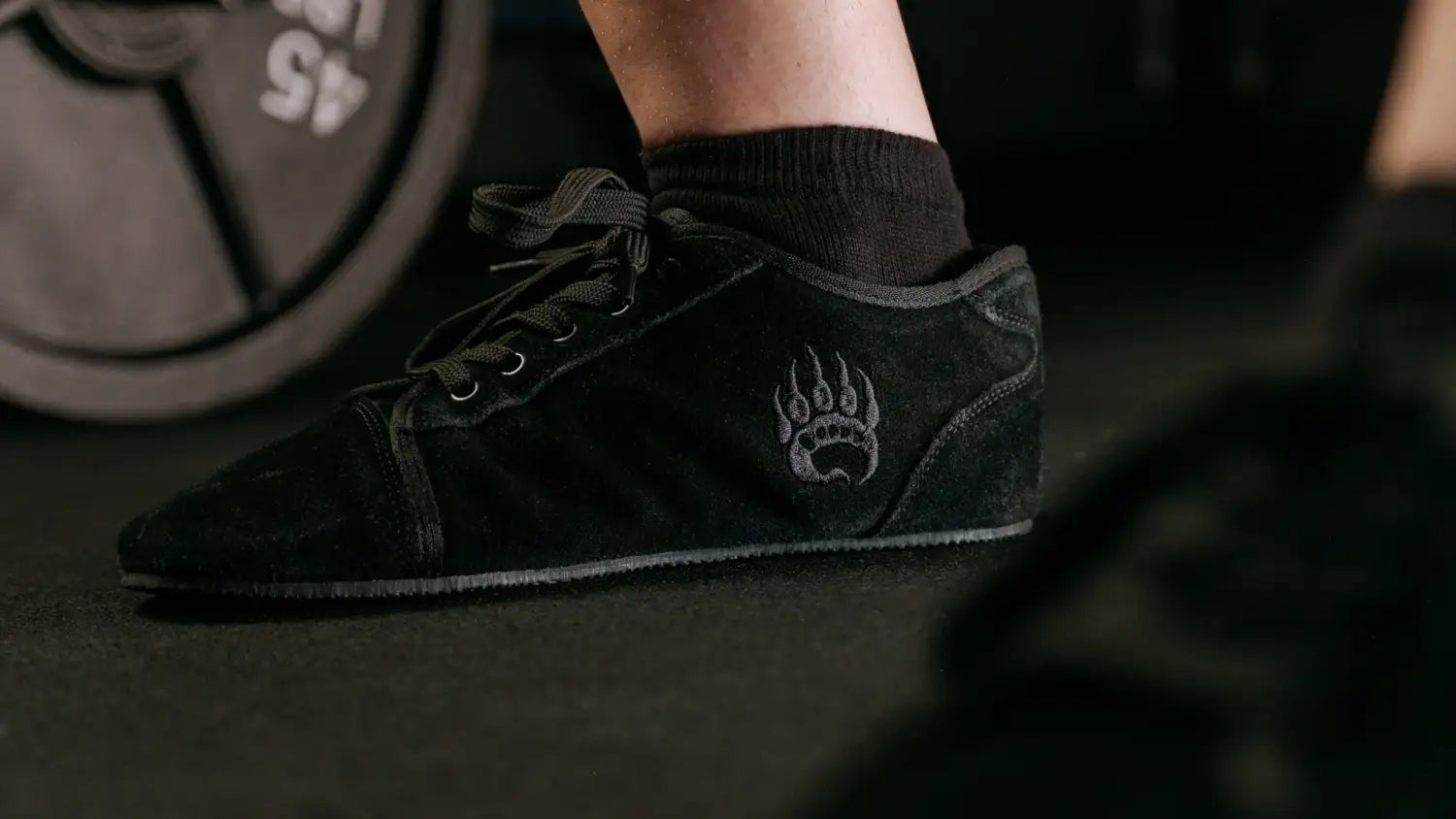 Black suede sneaker with a gray paw print logo on the side.