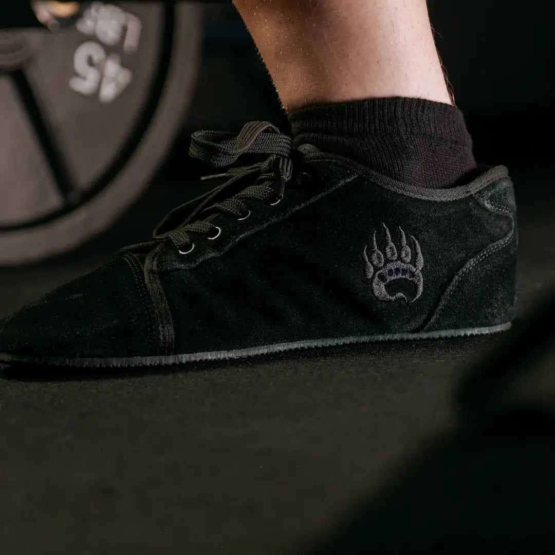 Black suede sneaker with a subtle embroidered paw print logo on the side.