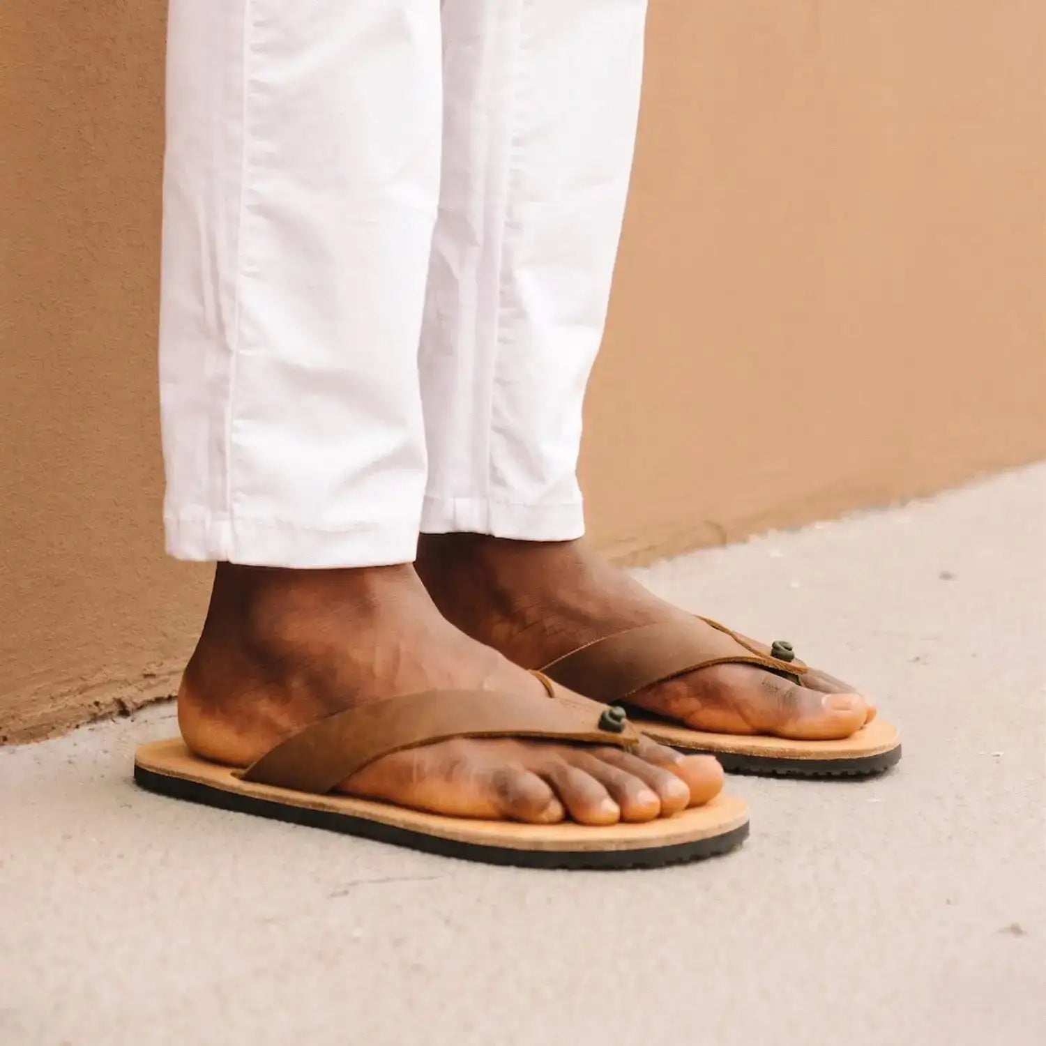 Brown leather flip-flops with a tan sole and black rubber edge, featuring small green rivets on the straps.