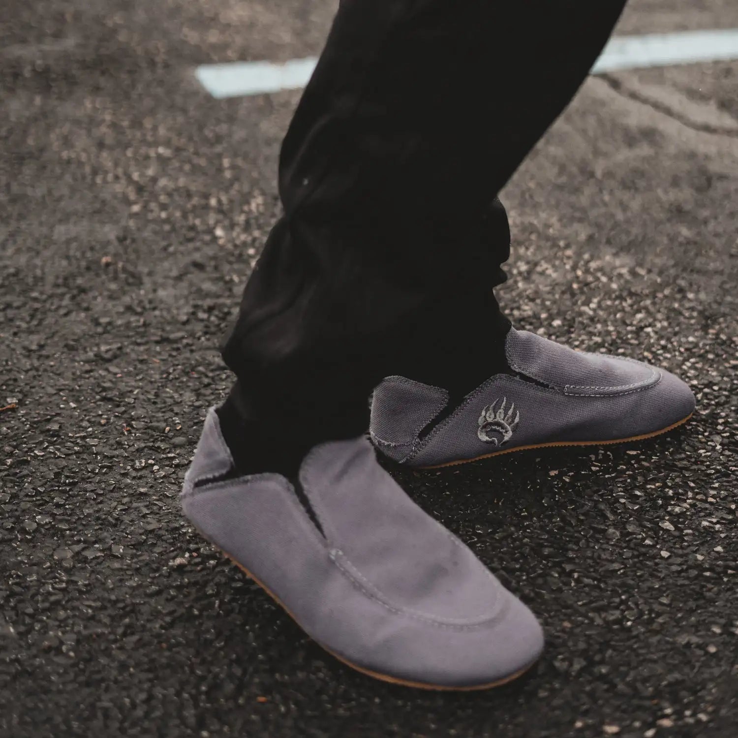 Gray suede slip-on shoes with a subtle embroidered paw print logo on the side.