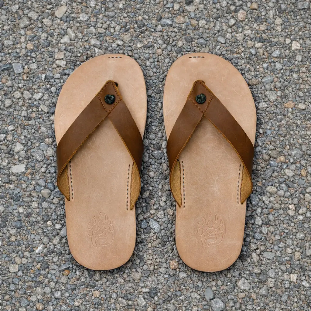 Tan leather flip-flops with brown straps and a subtle embossed paw print on the sole.