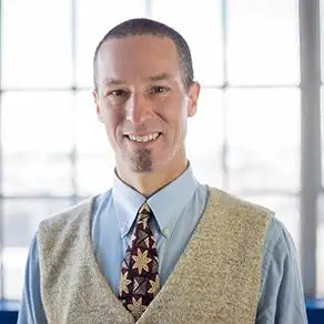 Tan sweater vest with blue shirt and patterned tie, likely wool or acrylic blend.